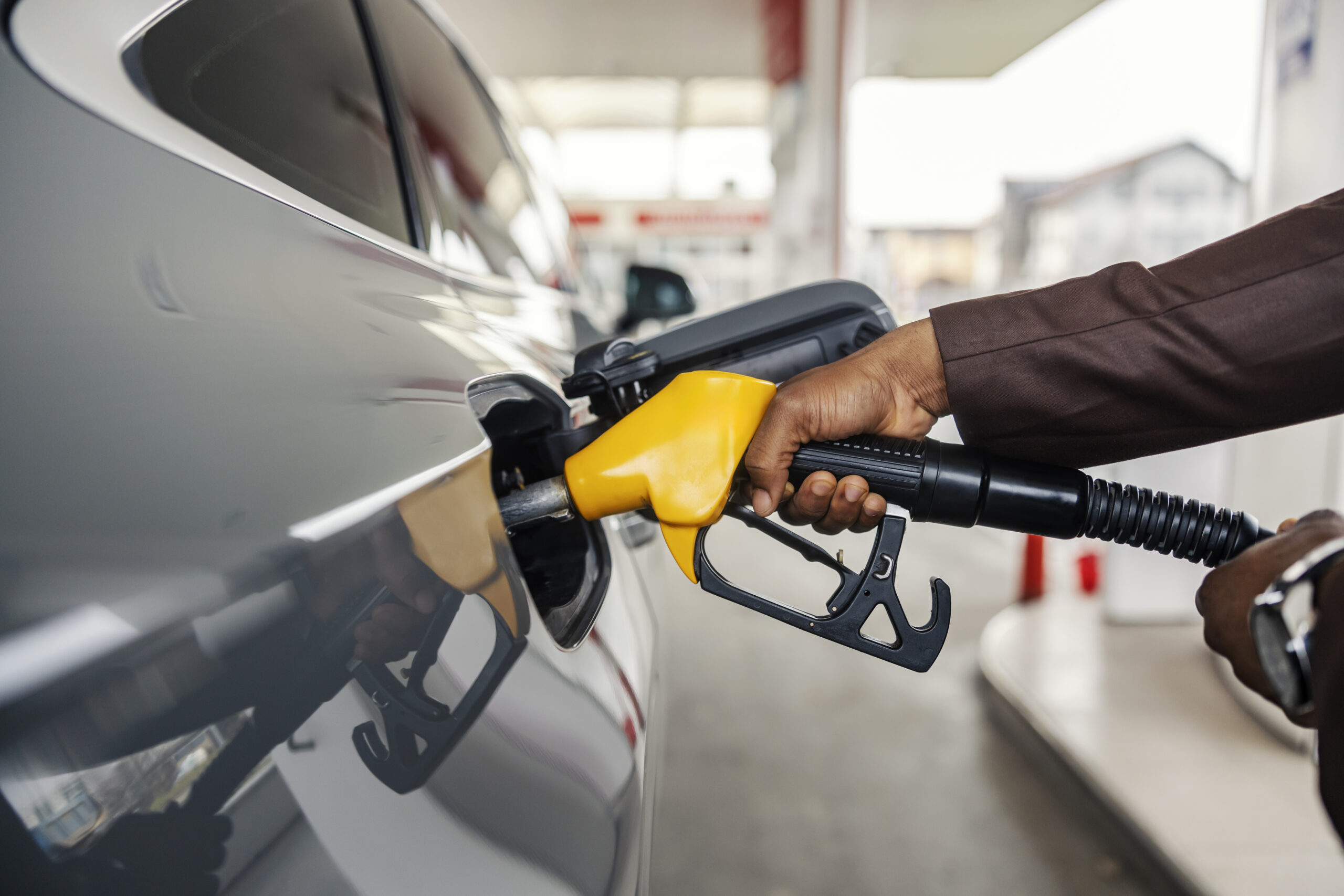 Une main tient un pistolet de carburant dans le réservoir d’une voiture.
